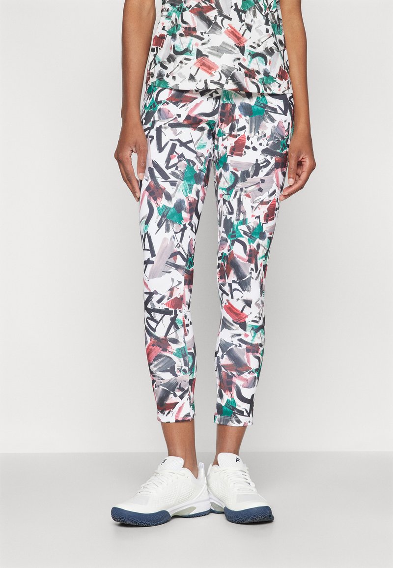 Capri-Leggings mit einem abstrakten, bunten Muster aus Rot, Grün und Schwarz auf weißem Hintergrund, kombiniert mit weißen Sportschuhen.
