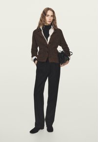 Hnědý kardigan ze směsi vlny přes černý rolák, doplněný pruhovanými černými kalhotami a malou černou kabelkou. Hladký materiál s dobře padnoucím střihem.