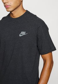 Black cotton t-shirt featuring a silver Nike logo on the left chest. Round neckline and short sleeves with a classic fit.