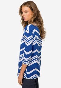 Niebieska i biała bluzka w wzór zygzaka, z rękawami o długości trzech ćwierci, wykonana z miękkiego materiału, z luźnym krojem i zaokrąglonym dołem.