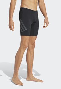 Bañador negro hecho de material elástico, con un diseño ajustado que presenta tres franjas grises a los lados.
