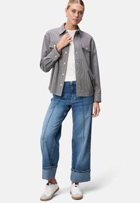 Grau karierte Hemdjacke mit Fronttaschen, getragen über einem weißen Top. Hellblaue weit geschnittene Jeans mit kontrastierenden Nähten und umgeschlagenen Säumen. Weiße Sneaker.