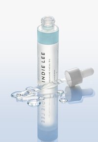 Przezroczysta szklana butelka z zakraplaczem z jasnoniebieską etykietą, zawierająca olejek do twarzy ze squalanem. Wyróżnia się białym zakraplaczem i rozproszonymi kroplami na odbijającej się powierzchni.