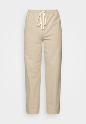 Pantalon beige en coton avec une taille élastique, un cordon ajustable et une coupe fuselée. Texture lisse, simple sans motifs ni accents.