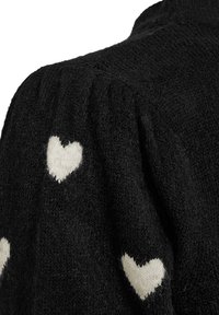 Svart stickad tröja med texturerad tyg och vita hjärtmönster. Detaljer inkluderar puffärmar och hög krage.
