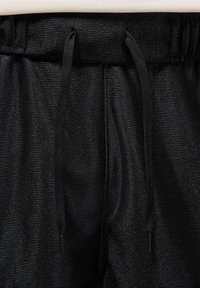 Shorts de sport noirs fabriqués dans un tissu texturé et brillant, avec une taille à cordon de serrage et deux coutures verticales. Design simple et fonctionnel.