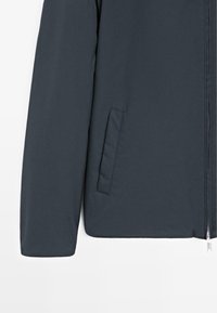 Dunkelgraue Jacke mit glatter Textur, ausgestattet mit einem Reißverschluss und einer Seitentasche. Die Ärmel sind breit und leicht gepolstert.