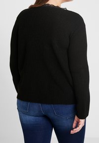 Suéter negro de punto acanalado con un escote decorado con encaje, con mangas largas y un corte relajado, combinado con jeans de mezclilla azules.