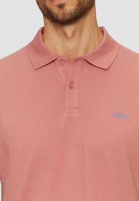 Koszula polo z krótkim rękawem w jasnoróżowym kolorze, wykonana z teksturowanej tkaniny. Posiada klasyczny kołnierzyk, dwa guziki oraz niebieskie logo "s.Oliver".