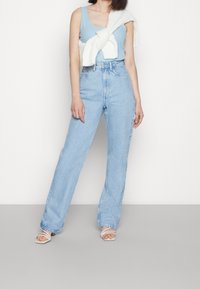 Light blue ribbed tank top, white knit sweater draped over shoulders, high-waisted light blue jeans, and white heeled sandals.