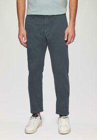 Chinos gris foncé avec une coupe slim, en tissu de coton doux. Présente un design épuré, des poches latérales et est associée à des baskets blanches.