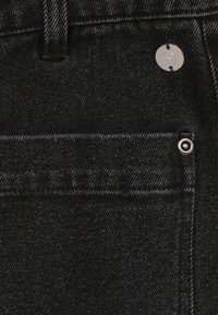 Zwarte denim jeans met een gladde textuur, voorzien van een voorzak en zilverkleurige hardware. De stiksels zijn zichtbaar langs de naden voor extra detail.