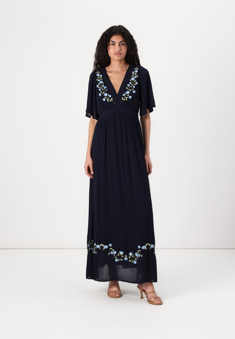 Long navy dress featuring floral embroidery in light blue and green along the neckline and hem, with short sleeves and a flowing design.