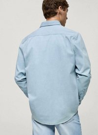 Camicia di jeans azzurra chiara con design colletto, maniche lunghe e polsini con bottone, dalla texture liscia e orlo arrotondato.
