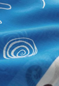 Tissu bleu avec des motifs en spirale blancs et des ombres subtiles, montrant des plis et une texture dans une lumière douce et naturelle.