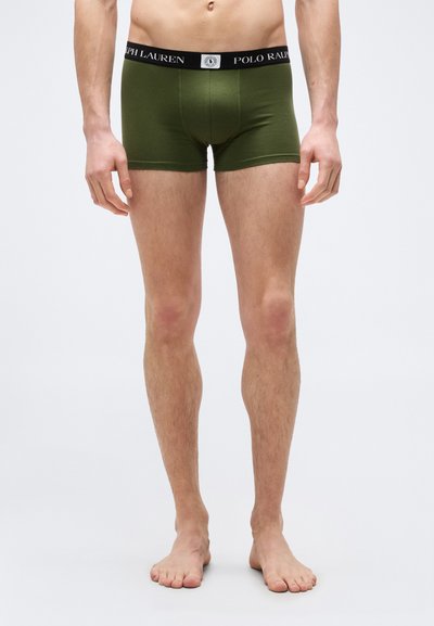 Άνδρας μοντέλο που φοράει εσώρουχα τύπου boxer σε ελιά πράσινο χρώμα με μαύρη μέση που φέρει την επιγραφή "Polo Ralph Lauren", όρθιος ξυπόλητος μπροστά σε απλό λευκό φόντο.