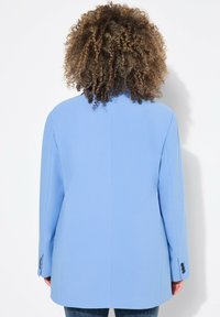 Blazer bleu clair avec un design structuré, fente centrale et poignets à quatre boutons. Tissu lisse avec une coupe ajustée. Vue arrière montrée.