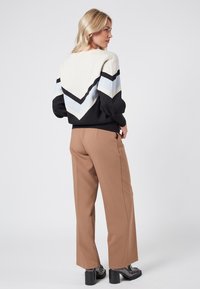 Color-blocked sweater featuring black, gray, and light blue zigzag patterns. Paired with beige pants and chunky black platform shoes.