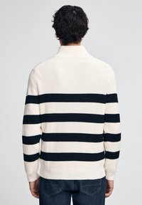 Strickpullover mit vertikalen schwarz-weißen Streifen, ausgestattet mit einem gerippten Kragen und Bündchen. Der Stoff wirkt weich und strukturiert.