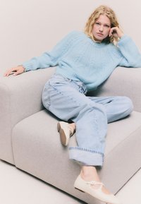 Šviesiai mėlynas megztinis su tekstūriniu raštu, derinamas su šviesiai džinsais. Modelis dėvi smėlio spalvos balerinas su dirželiu ir maža sagtimi.