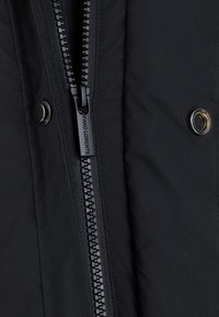 Czarna pikowana kurtka z centralnym zamkiem błyskawicznym i zapięciem na napy, o gładkiej fakturze i subtelnym logo na uchwycie zamka.