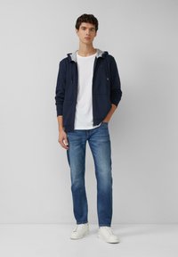Granatowy rozpinany bluza z szarym podszyciem, zestawiona z białą koszulką i jasnoniebieskimi dżinsami. Białe sneakersy dopełniają casualowy strój.