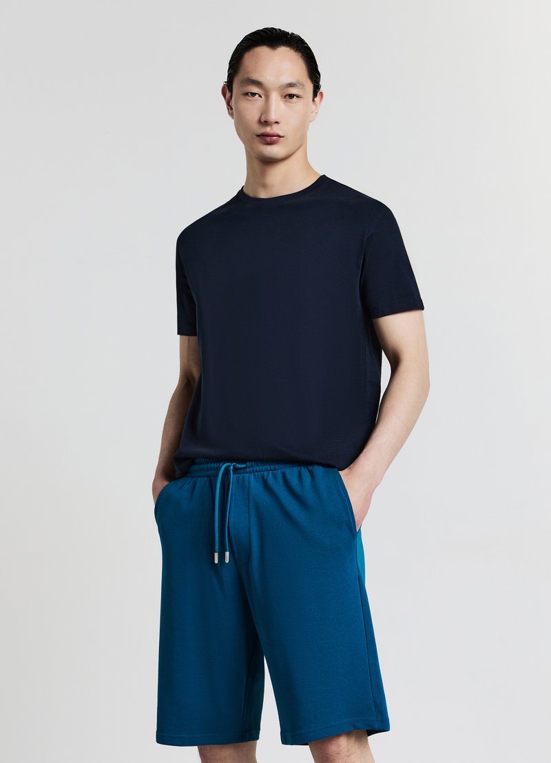 T-shirt a maniche corte blu navy abbinata a pantaloncini con coulisse color turchese. Il tessuto sembra morbido con una texture liscia; i pantaloncini hanno tasche laterali.