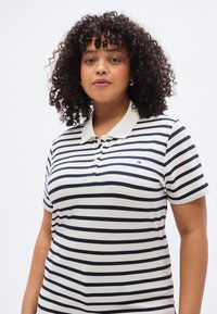 Πολυτελές πόλο μπλουζάκι με ρίγες σε εκρού και ναυτικό μπλε, με γιακά, κοντά μανίκια, τρεις κουμπιολωρίδες και μικρό κεντημένο λογότυπο.