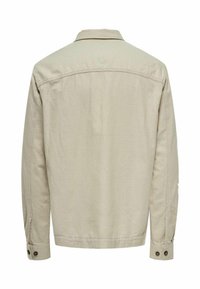 Chemise beige à manches longues avec col, poignets à boutons et texture unie. Présente une coupe droite sans motifs ni embellissements visibles.
