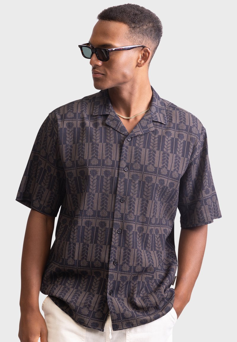 Camicia a maniche corte di un blu navy scuro con un motivo decorativo di linee verticali e motivi floreali. Presenta una vestibilità rilassata e chiusura con bottoni.