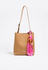 Tan leather tote bag with a smooth texture, featuring a long strap and a pink scarf accent attached to the handle. Brand logo displayed.