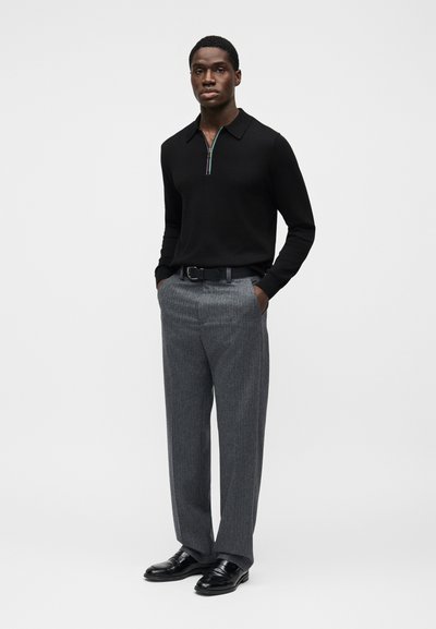 Μαύρο πόλο πουκάμισο με φερμουάρ και γιακά, συνδυασμένο με γκρι πλισέ παντελόνι και μαύρα δερμάτινα παπούτσια. Απλός σχεδιασμός με διακριτή υφή.