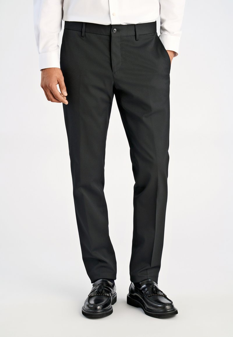 Czarne dopasowane spodnie eleganckie o gładkiej fakturze, z przednimi kieszeniami i zapięciem na jeden guzik, w połączeniu z błyszczącymi czarnymi butami.