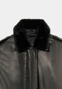 Giacca nera in pelle con colletto in pelliccia sintetica, caratterizzata da una texture liscia, chiusure con bottoni e un design minimalista.