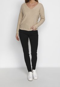 Beige v-halsad tröja med långa ärmar, tillsammans med svarta åtsittande byxor och vita sneakers. Mjuk textur och avslappnad passform.