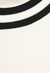 Close-up of white knit fabric with black ribbed trim featuring two concentric stripes near the neckline.