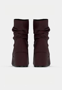 Paire de bottines marron foncé décontractées avec talons blocs vue de dos sur un fond clair uni.