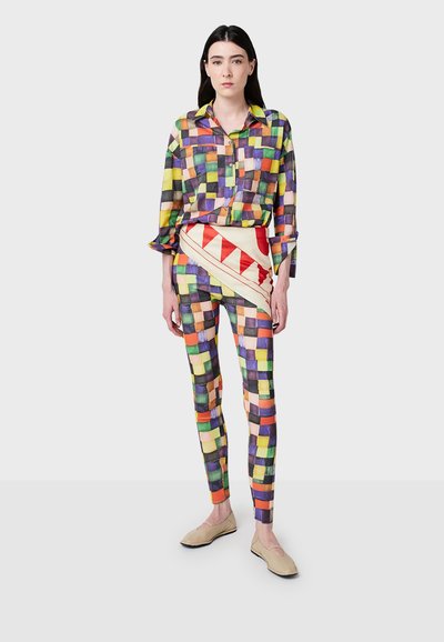 Chemise à carreaux multicolores à manches longues et fermeture à boutons, associée à des leggings à motifs avec des designs géométriques dans des couleurs vives.