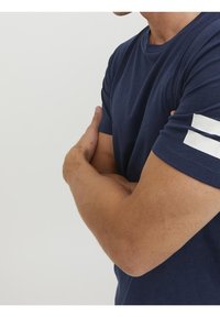 Camiseta de manga corta azul marino de algodón, con rayas blancas en el hombro izquierdo. Cuello redondo y diseño ajustado con costuras visibles.