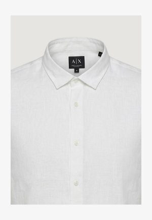 Chemise blanche en lin à manches longues avec col pointu et boutons blancs, étiquette indiquant la marque A|X Armani Exchange et la taille moyenne.
