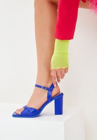 Sandalo con tacco alto in pelle blu, con punta quadrata, design annodato, cinturino alla caviglia regolabile e tacco spesso.