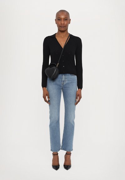 Black knit cardigan with V-neck and button closure, paired with light blue straight-leg jeans and black pointed-toe heels, carrying a heart-shaped bag.