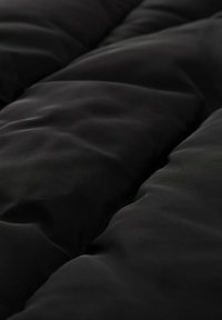 Conforter noir matelassé avec une texture lisse, présentant des poches de rembourrage qui créent une apparence en couches et un léger éclat sur le tissu.