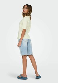 T-shirt de couleur crème à manches courtes, associé à un short en denim bleu clair avec un ourlet effiloché. Modèle portant des sandales plates-formes bleues.
