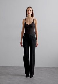 Svart ribbad tanktop tillsammans med skräddarsydda svarta byxor med knappar på fickorna. Slät textil och rak bendesign.