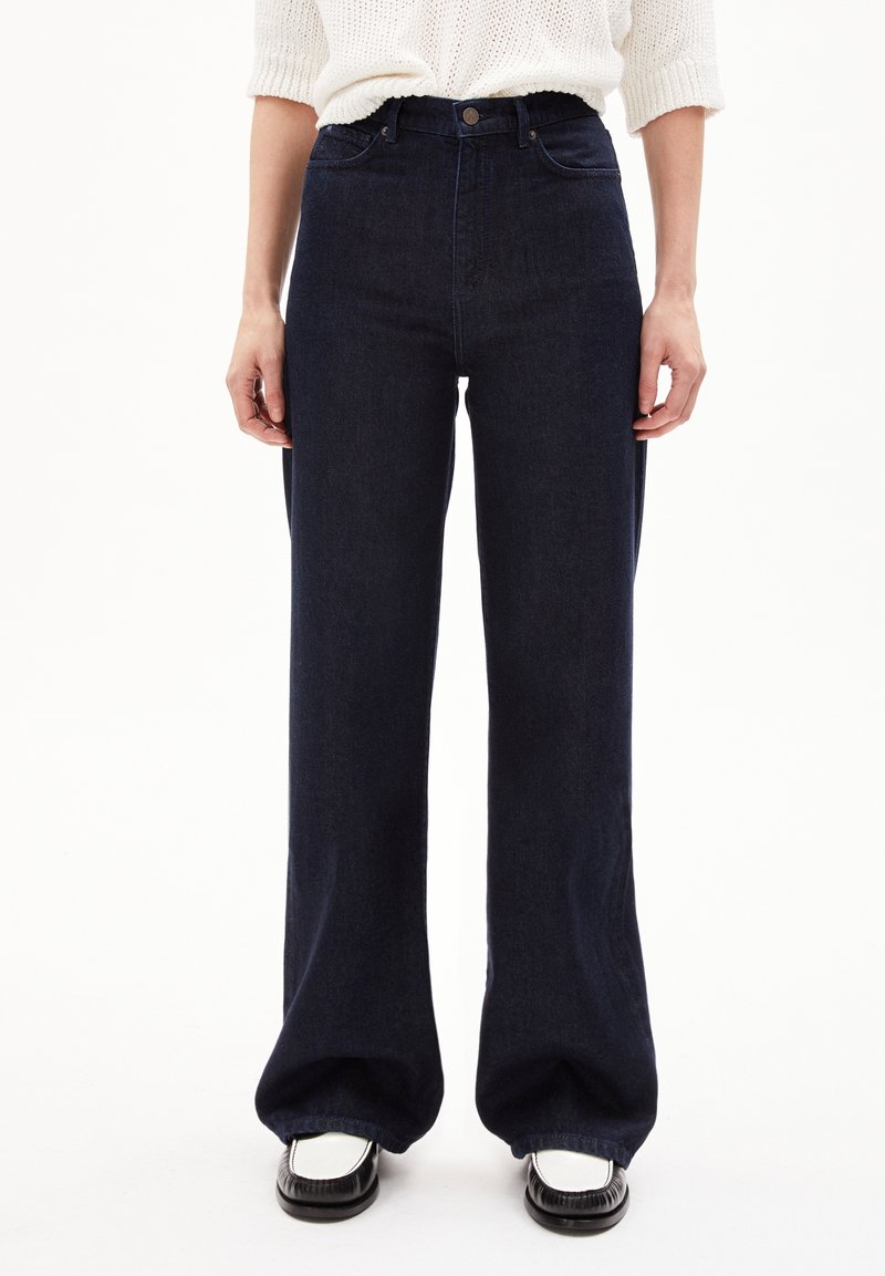 Jean taille haute, coupe large en denim indigo foncé. Caractéristiques d'un style classique à cinq poches et d'une fermeture à bouton. Tissu lisse et texturé.