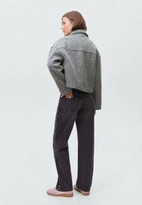 Veste courte en laine grise avec un col haut, assortie à un jean foncé avec des clous sur les côtés et des baskets roses. Design simple et fonctionnel.