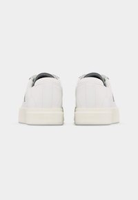 Ζευγάρι λευκών αθλητικών παπουτσιών χαμηλού ύφους με παχιά σόλα, από την πίσω πλευρά, με διακριτική σήμανση Calvin Klein στη φτέρνα.