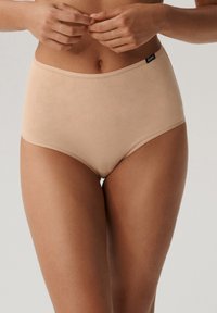 Beżowe figi z wysokim stanem wykonane z miękkiego materiału o gładkiej fakturze; posiadają subtelny metkowany logo na pasku w celu identyfikacji marki.