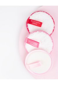 Tres discos redondos para limpiar en distintos tonos de rosa con superficies blancas y suaves. Las etiquetas dicen "RETIRAR", "LIMPIAR" y "EXFOLIAR".